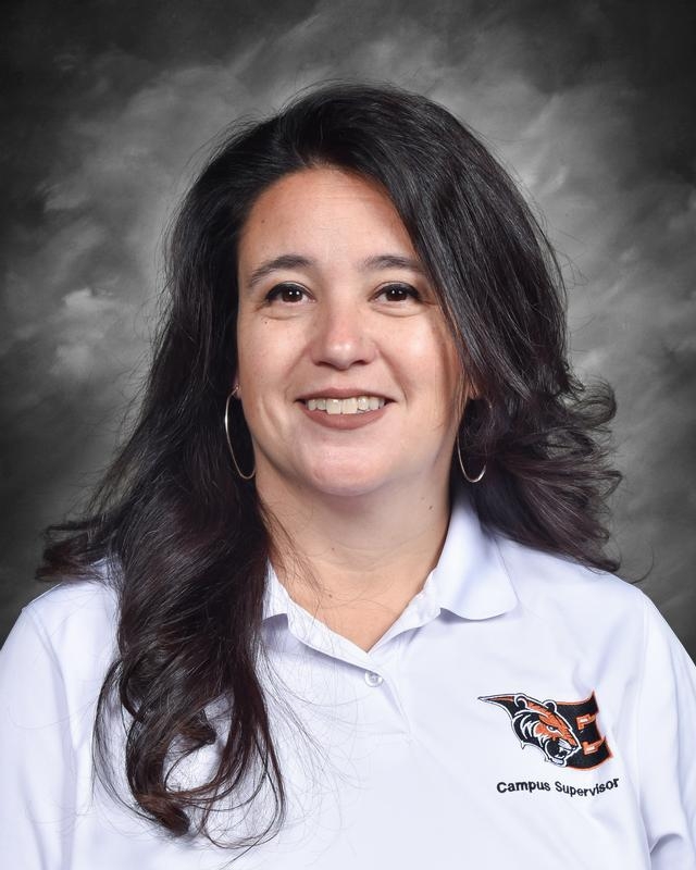 A woman with long, dark hair smiles, wearing a white polo shirt with a tiger logo and "Campus Supervisor" text.