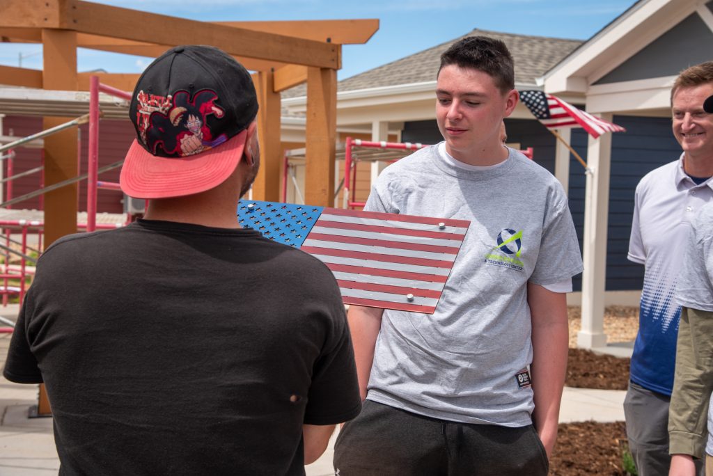 A CETC student gifts a veteran a handcrafted, metal flag he created while his teacher looks on